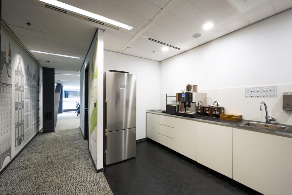 Modern office kitchenette with a coffee machine, sink, and stainless steel refrigerator at Jacob Bontiusplaats.
